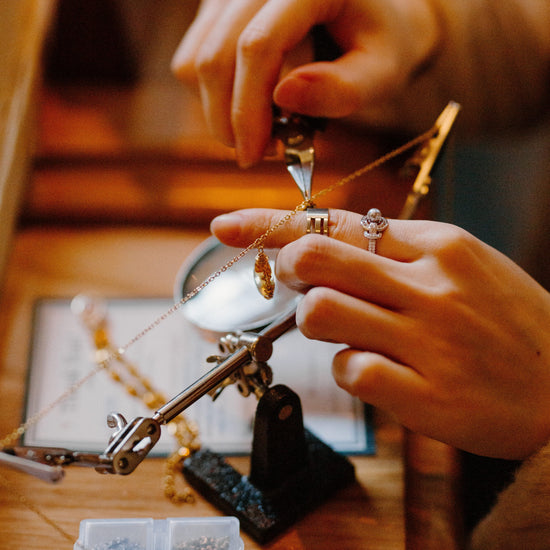 Person working on jewelry with tools and materials on a wooden table